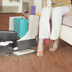 Eine Person sitzt in einem Zimmer mit Papiertüten und einem rot-braunen Vinylboden in Holzptik