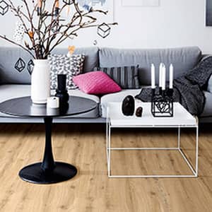 Heller Vinylboden in einem Wohnzimmer mit einem hellgrauen Sofa, einem schwarzen runden Couchtisch und einem Weißen quadratischen Couchtisch